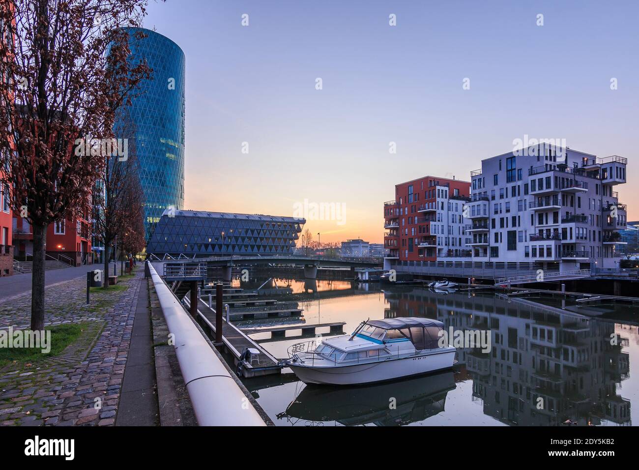 Stadtbild in Frankfurt am Main mit Kanal und Gebäuden. Boote im Hafen vor Sonnenaufgang im West Harbour Wohngebiet. Straße mit Bäumen und r Stockfoto