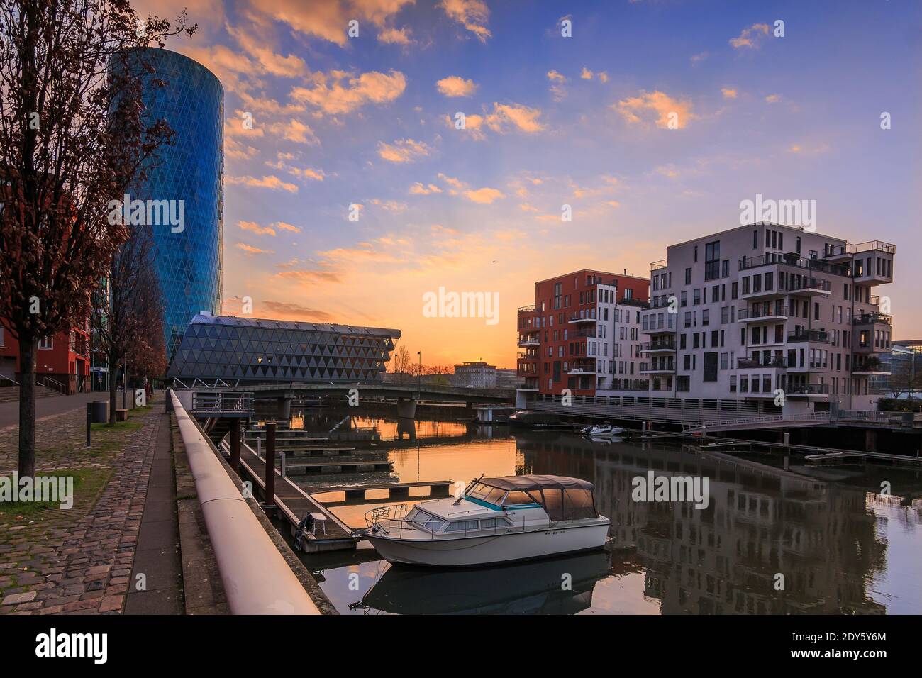 Sonnenaufgang über Westhafen mit Kanal vom Main in Frankfurt am Morgen und Wolken im Wohngebiet. Blauer Himmel und Straße mit Bäumen, Bank und Stockfoto