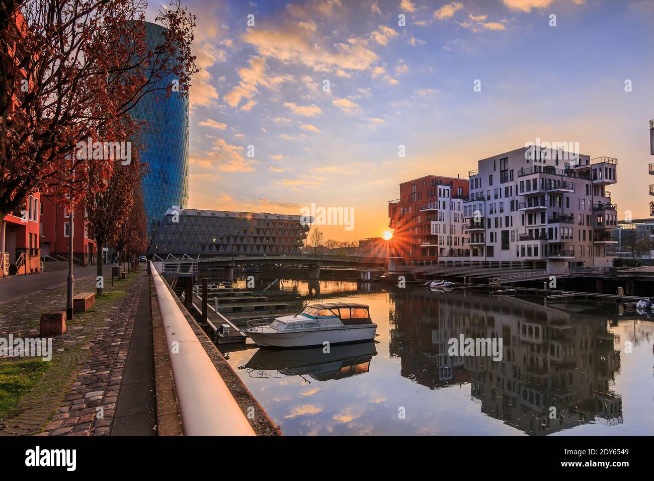Morgenstimmung in einem Wohngebiet. Sonnenaufgang mit Sonnenstrahlen zwischen den Gebäuden. Flusslauf im Westhafen der Stadt Frankfurt. Straße Stockfoto
