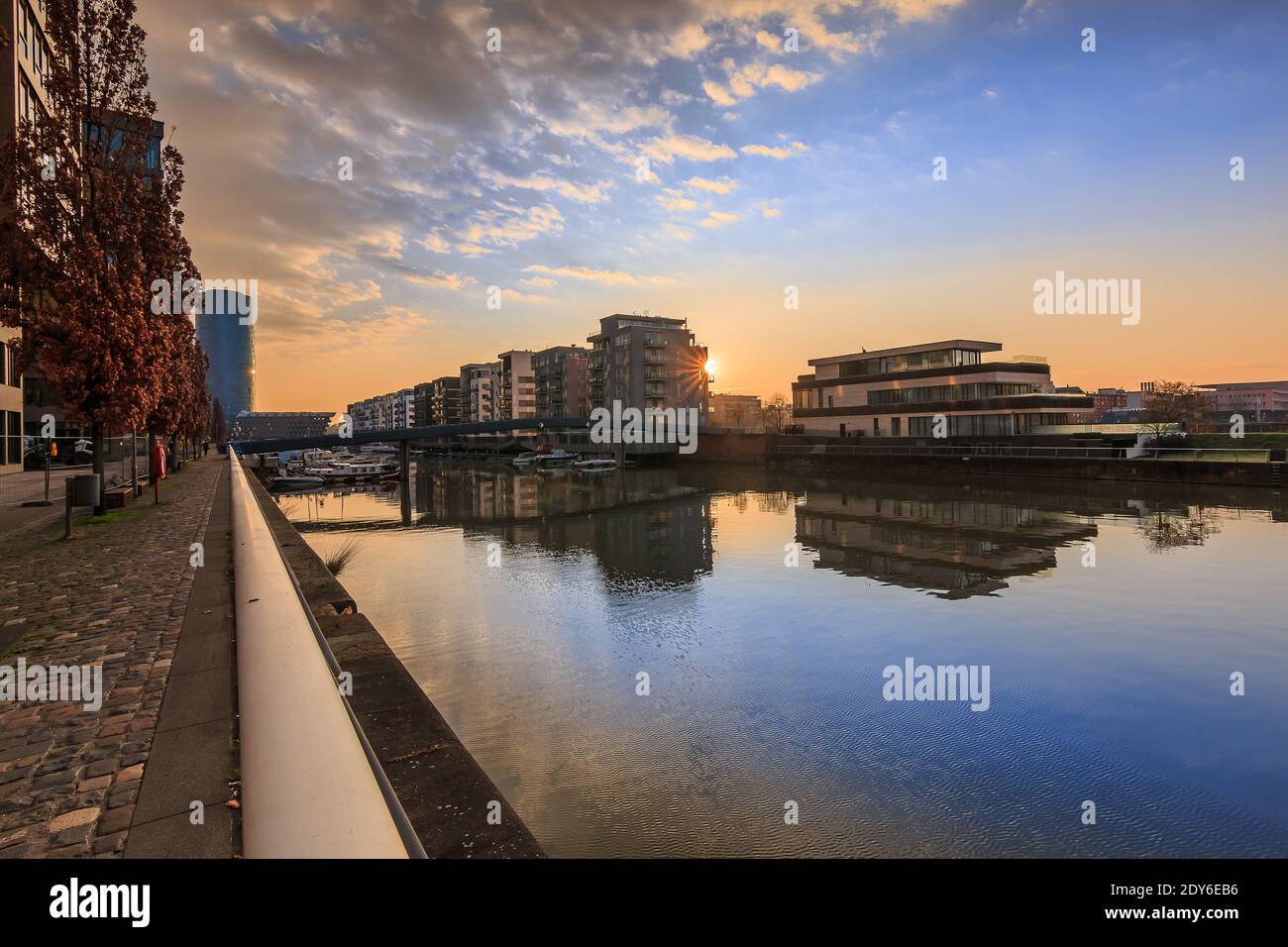 Kanal vom Main am Morgen. Wohngebiet in Frankfurt bei Sonnenaufgang. Wasserfront mit Reflexion. Blauer Himmel und Wolken. Ufer im Hafen an Stockfoto