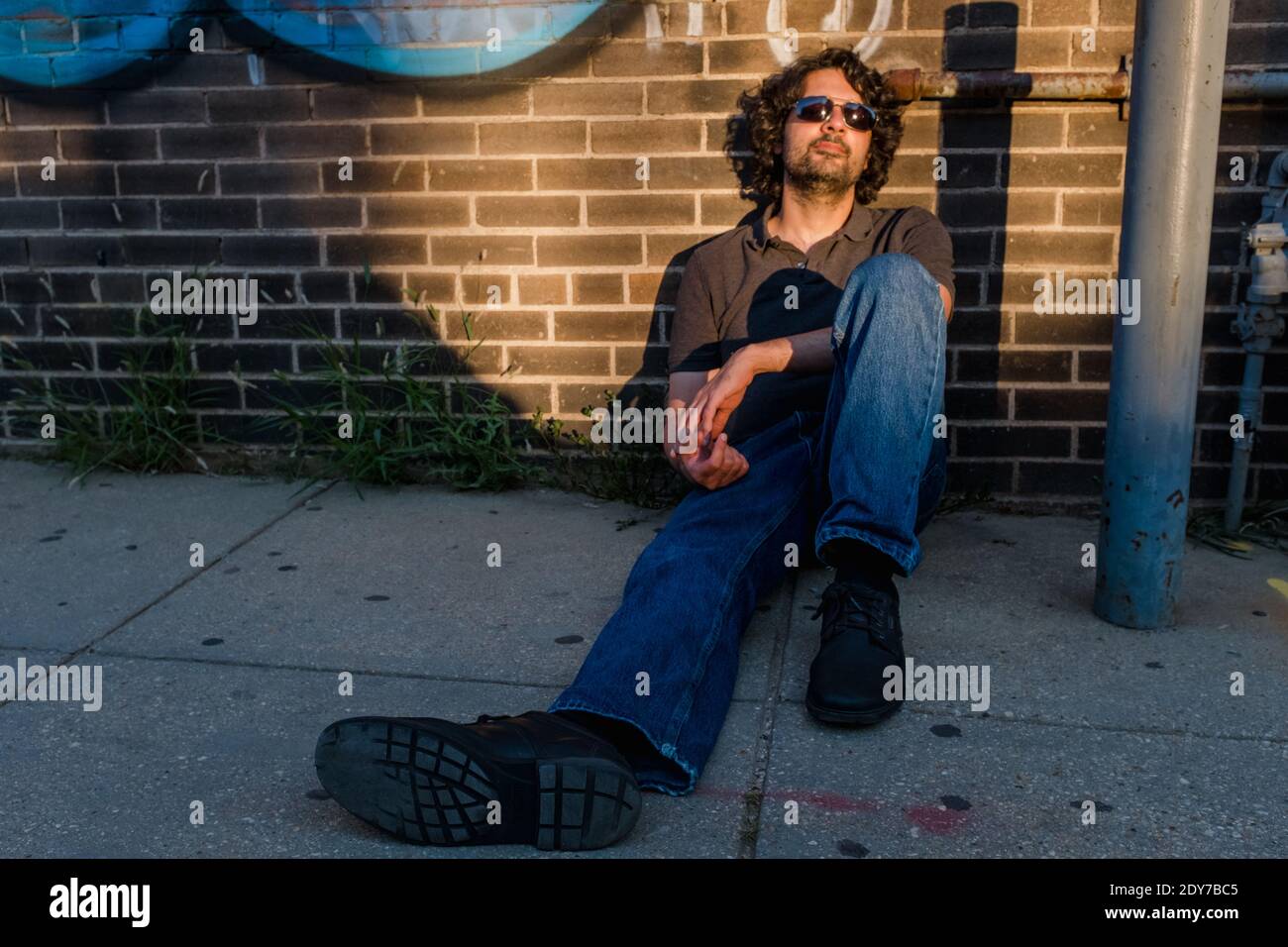 Porträt eines Mannes, der mit entspannter Haltung auf dem Bürgersteig der Stadt sitzt Stockfoto