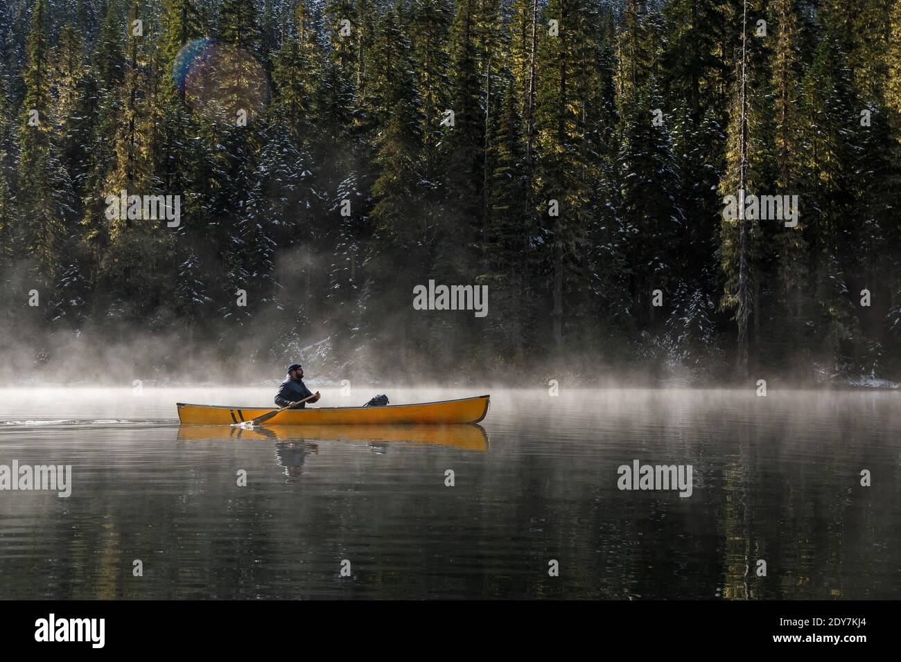Mann in einem Kanu auf einem nebligen See auf sonnig Tag umgeben von Bäumen Stockfoto