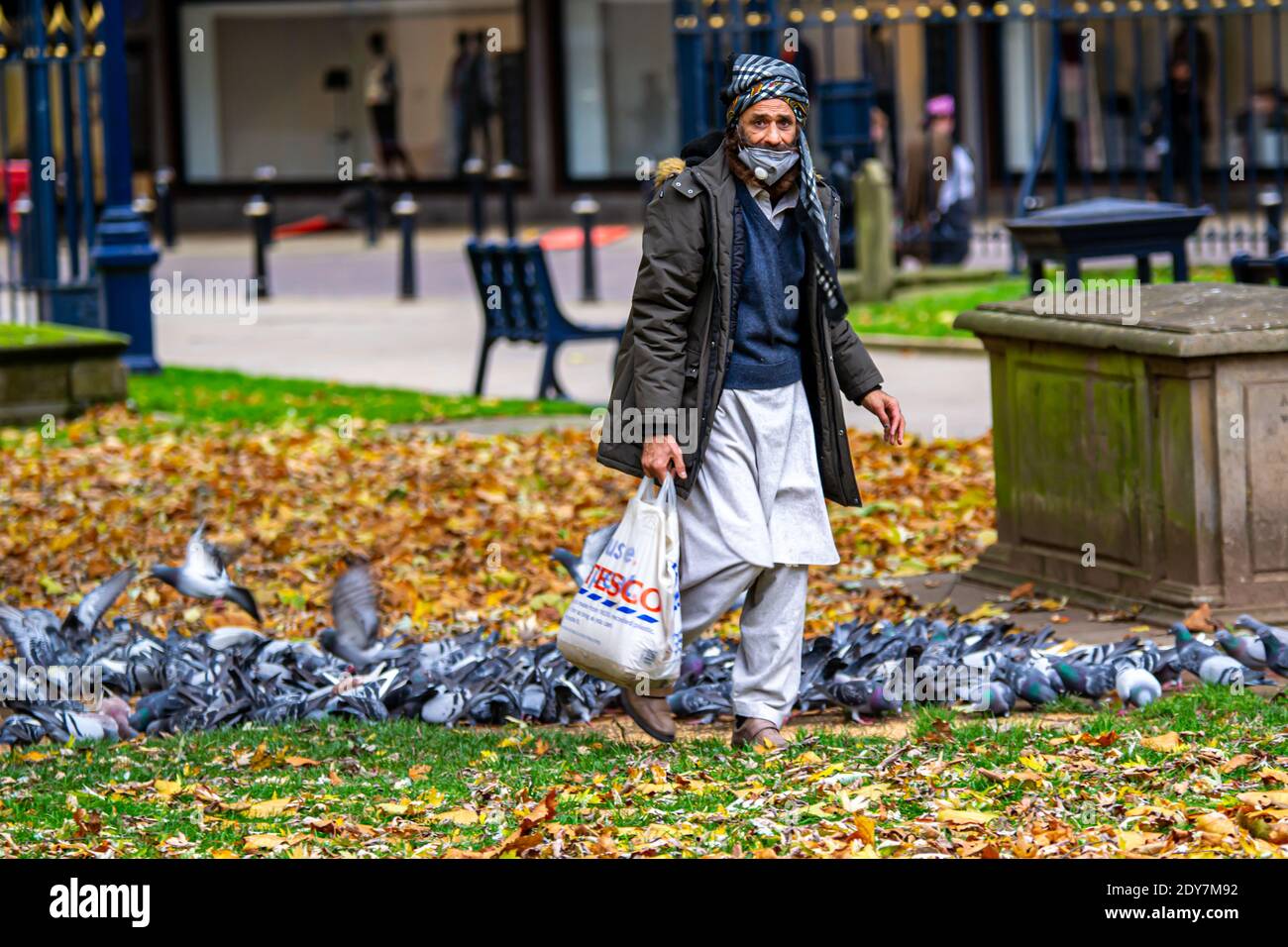 Asiatischer Mann unter den Tauben, mit Tesco Einkaufstasche in Birmingham, Großbritannien Stockfoto