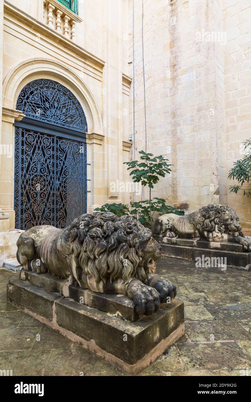 Geschnitzte Kalkstein Löwen Skulpturen und gewölbte Eingangstür mit verzierten schmiedeeisernen Grills, Garten des Grand Masters Palace, Valletta, Malta Stockfoto