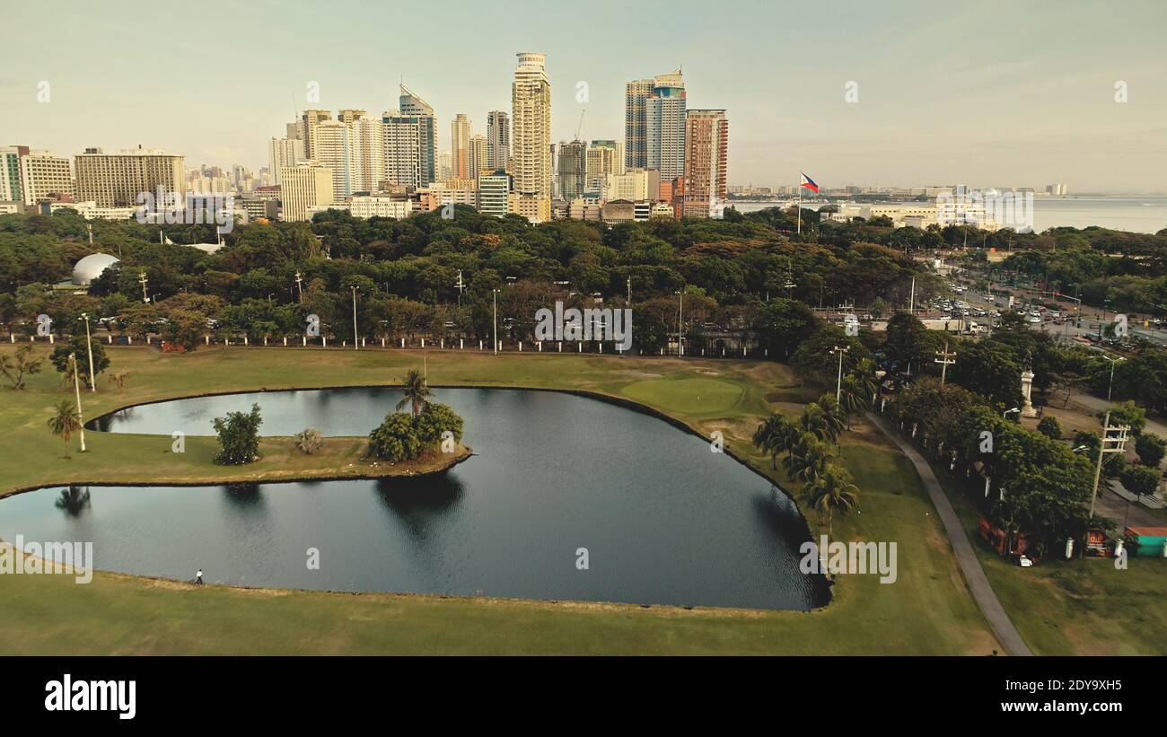 Gestaltete Parklandschaft am Teichufer Antenne. Grünes Gras Tal mit Blumen. Moderne Wolkenkratzer über grünen tropischen Pflanzen und Bäumen. Malerische Stadtlandschaft Natur von Manila Stadt, Philippinen, Asien Stockfoto