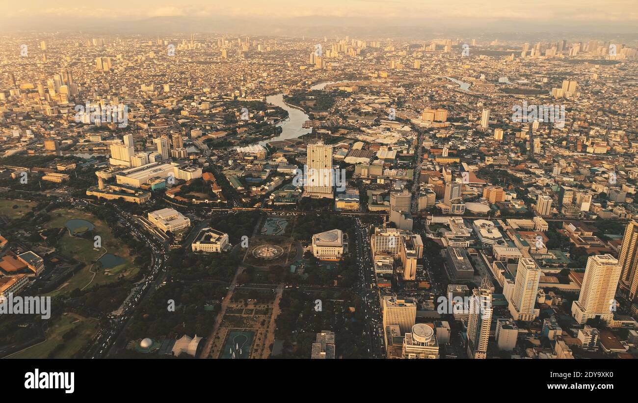 Entworfen Park an hohen Wolkenkratzern auf den Straßen der Stadt. Sonne scheint über Stadtbild mit Pflanzen, Bäumen. Philippinen Hauptstadt Manila. Filmisches Sonnenlicht bei modernen städtischen Gebäuden Luftbild Stockfoto