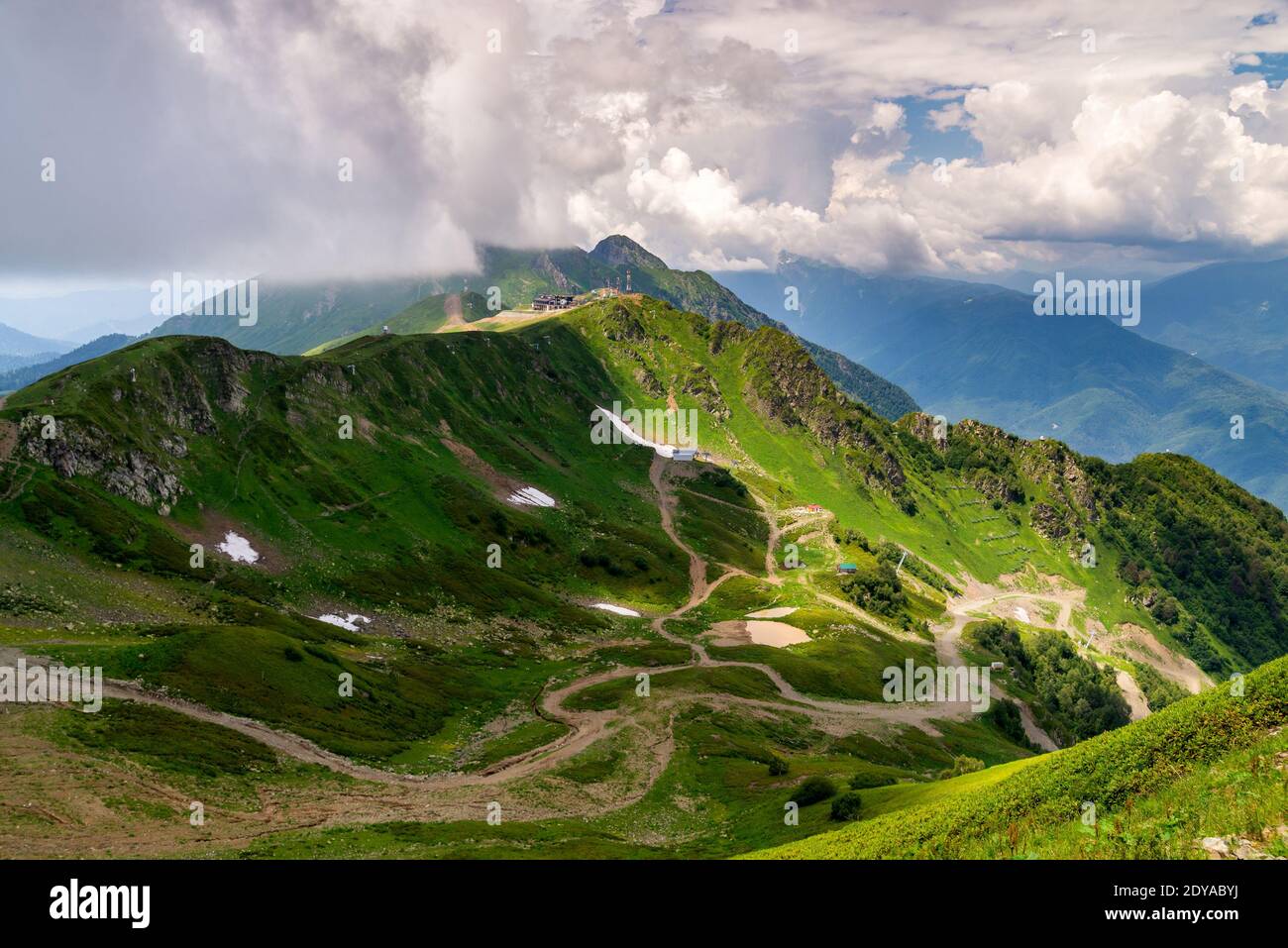 Landschaft von grünem Tal, bewaldeten Bergen und ein bisschen Schnee auf einem Gras. Stockfoto