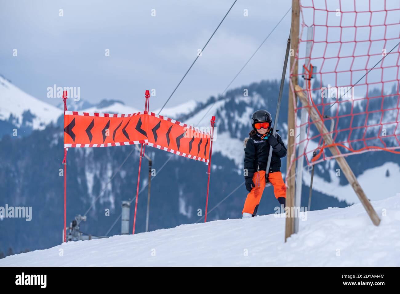 Skifahren im Schnee. Ein asiatisches Mädchen, das auf dem Skilift sitzt, indem es das Seil ergreifet und Skistöcke hält. Urlaub in der Schweiz. Frohe Kindheit. Stockfoto