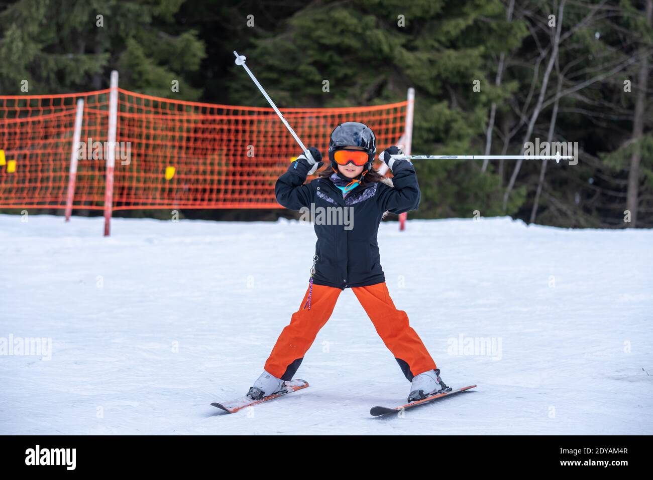 Skifahren im Schnee. Ein asiatisches Mädchen hält Skistöcke in den Händen. Urlaub in der Schweiz. Frohe Kindheit. Stockfoto