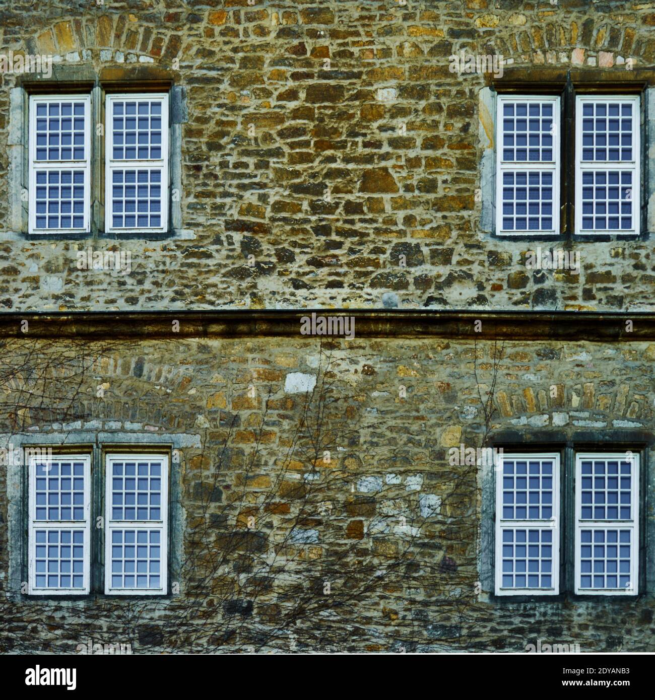 Hauswand aus groben Natursteinen mit vier Fenstern und einem geraden Gesims, abstrakt geometrisches Bild Stockfoto