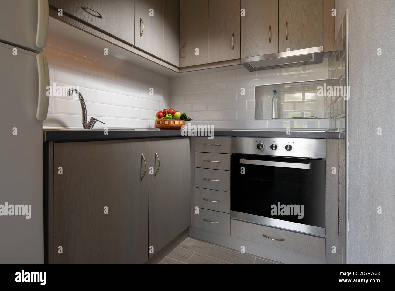 Modernes Interieur einer kleinen Eckküche mit weißen U-Bahn-Backsteinen. Obstteller auf hellem Holzschränke Hintergrund Stockfoto
