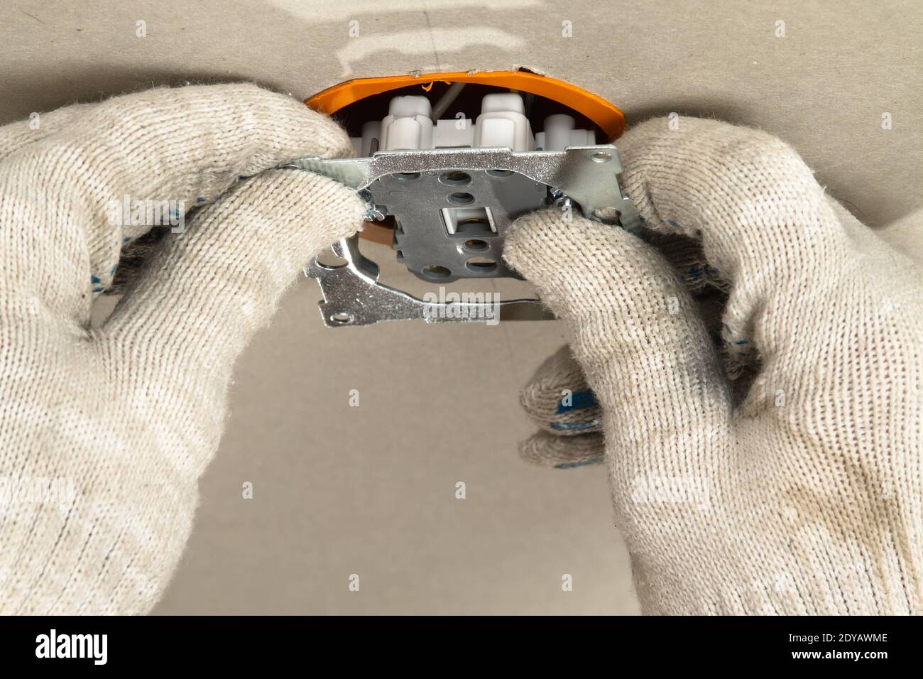 Die Hände eines Elektrikers stecken eine Steckdose in den ein Steckdosengehäuse an der Gipskartonwand Stockfoto