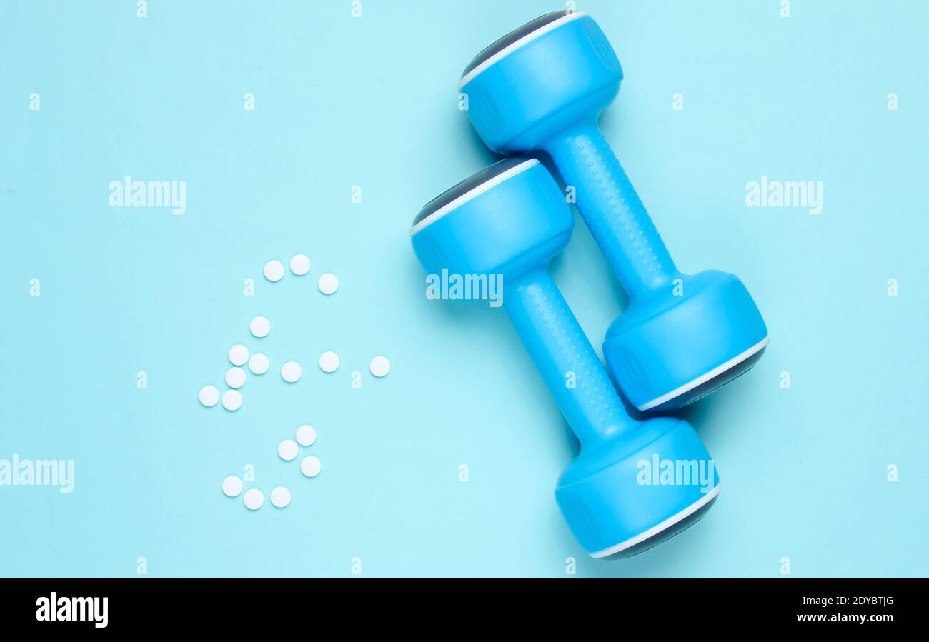 Sportapotheke. Kunststoff-Hanteln, Pillen auf blauem Hintergrund. Draufsicht. Stockfoto