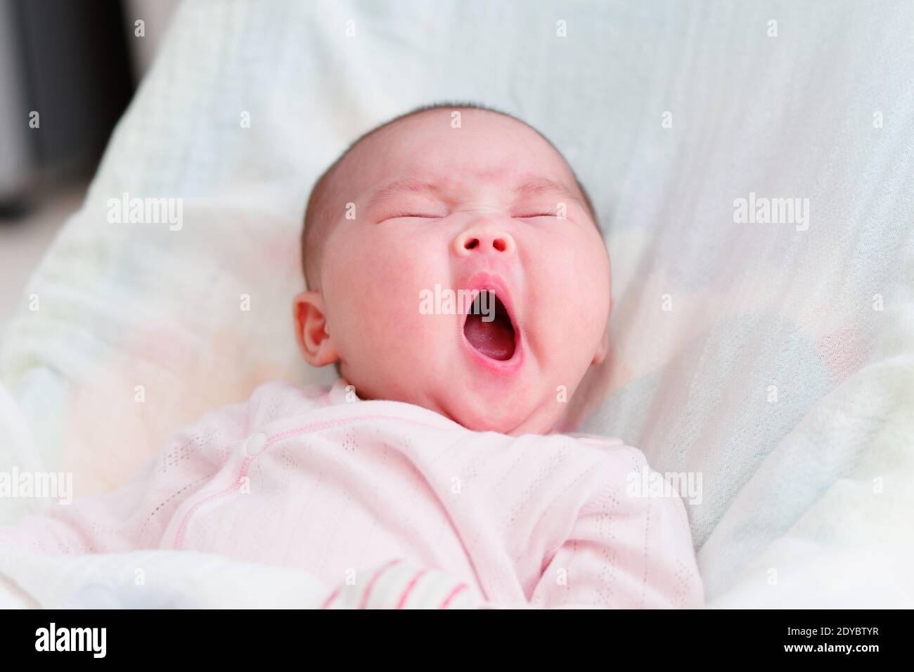 Chinesische Baby Mädchen neun Wochen alt schläfrig mit einem großen Gähnen. Noch keine Zähne. Stockfoto