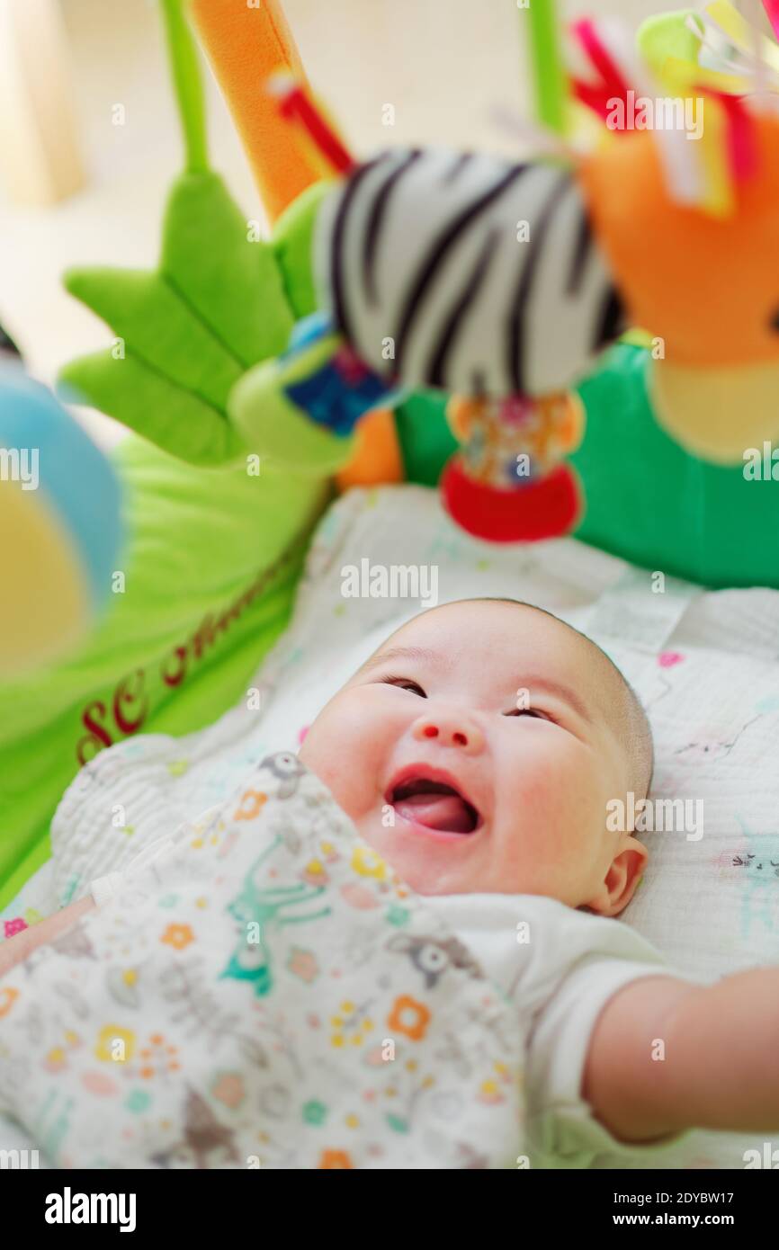 Drei Monate altes chinesisches Baby, das glücklich mit baumelnden Spielsachen über ihrem Bett spielt. Stockfoto