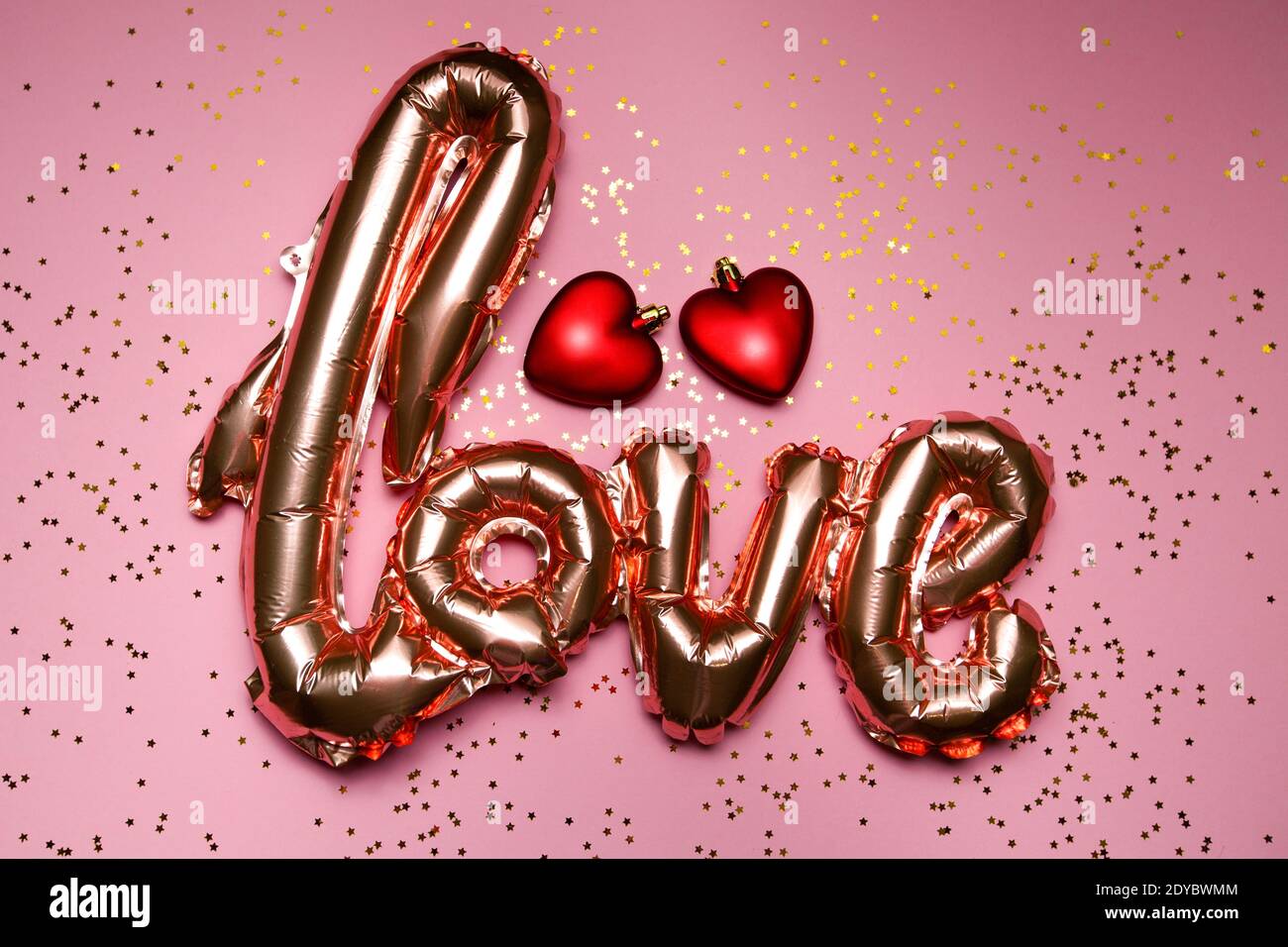 goldenes Wort Liebe mit roten Herzen auf rosa Hintergrund Stockfoto