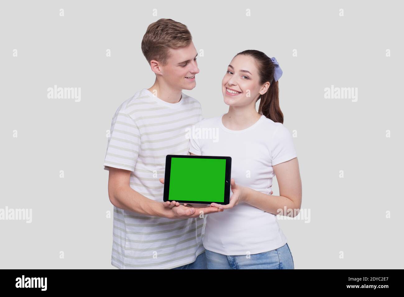 Paar zeigt Tablet Green Screen beobachten einander isoliert stehen. Konzept Für Werbung, Werbung Und Werbung Stockfoto