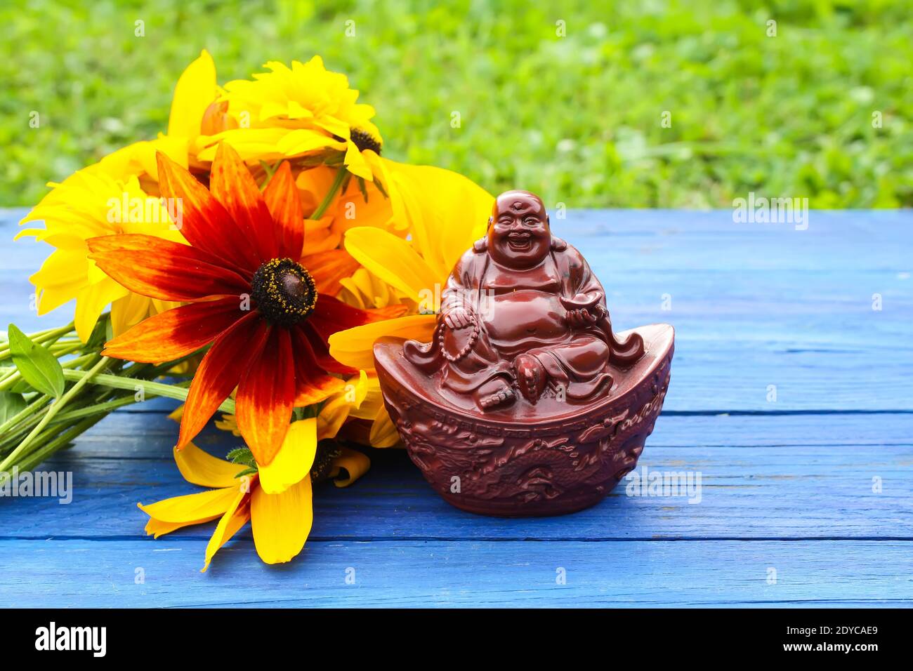 Keramik buddha Figur auf blau gealterten Holzbrettern im Sommerpark mit Rudbeckia Blumen. Stockfoto
