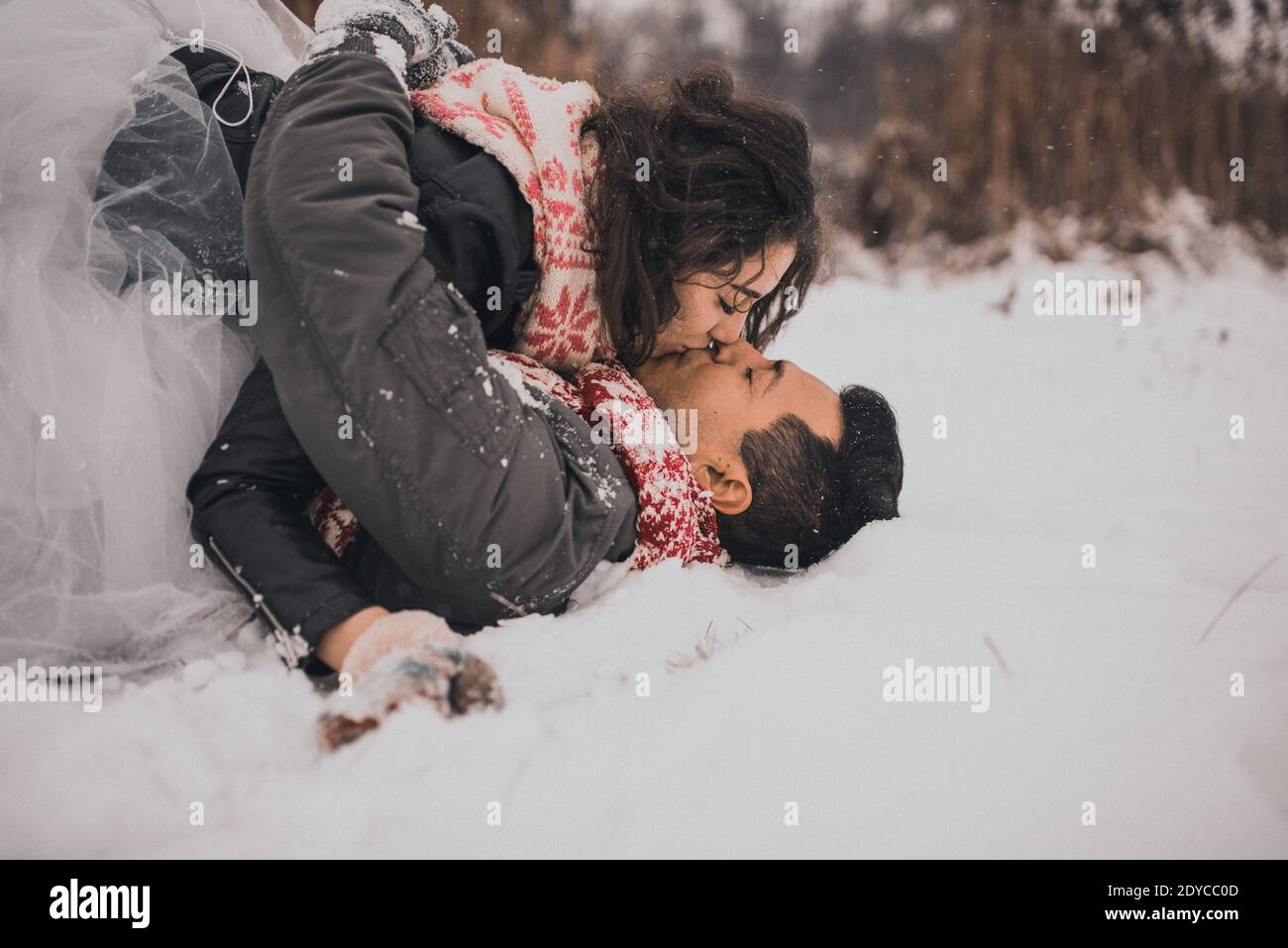 Junge Mann und Frau stehen küssen und umarmen. Braut und Bräutigam in Liebe Paar in gestrickten Schal und Fäustlinge im Winter mit Schnee und Schneeflocken. Hochzeit Stockfoto