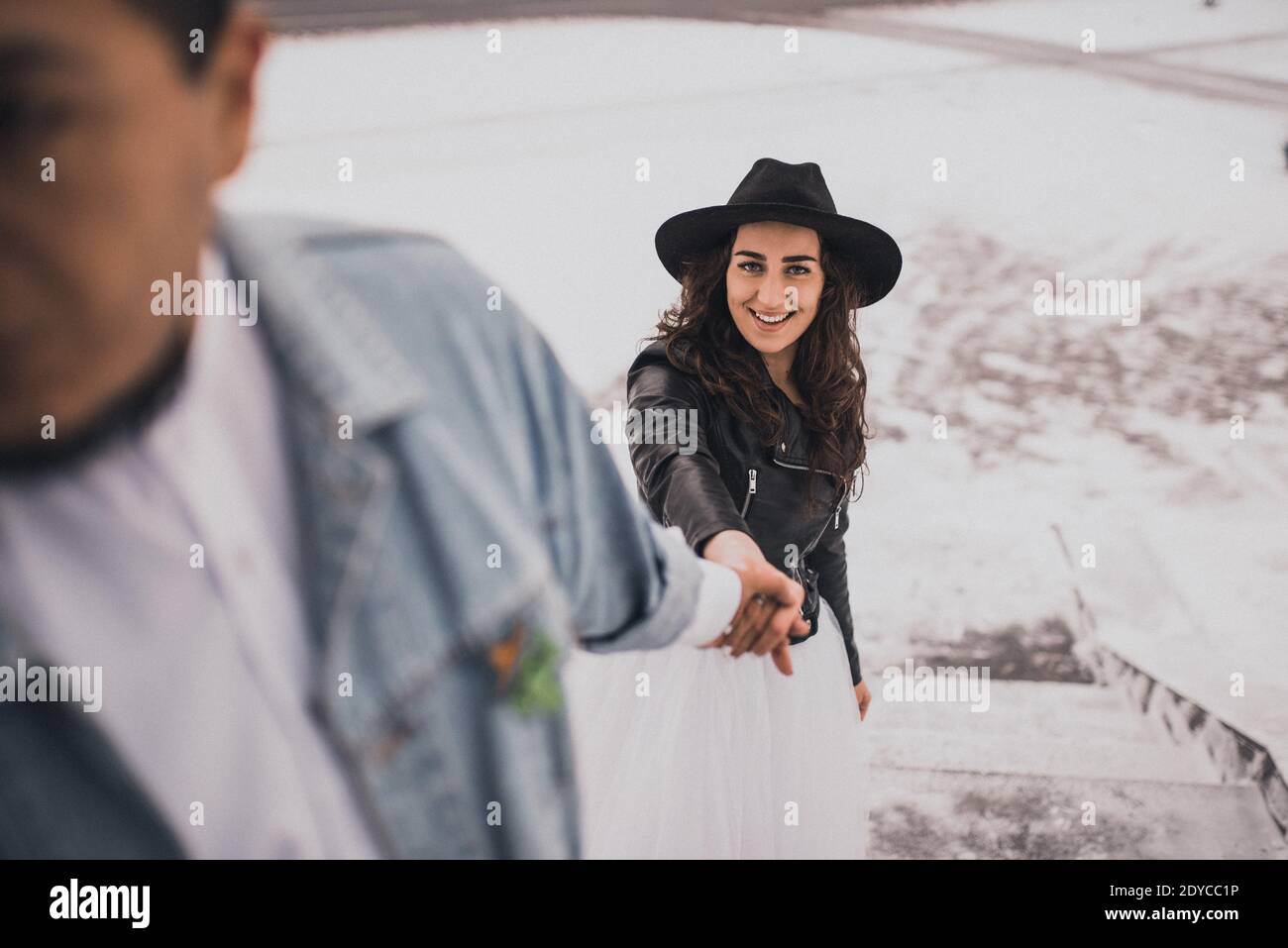 Mexikanischer hispanischer Mann in übergroßer Jeansjacke und Frau in hut Leder Biker Jacke küssen Umarmung lachend walking.groom Braut Hochzeit Ich liebe das Paar Stockfoto