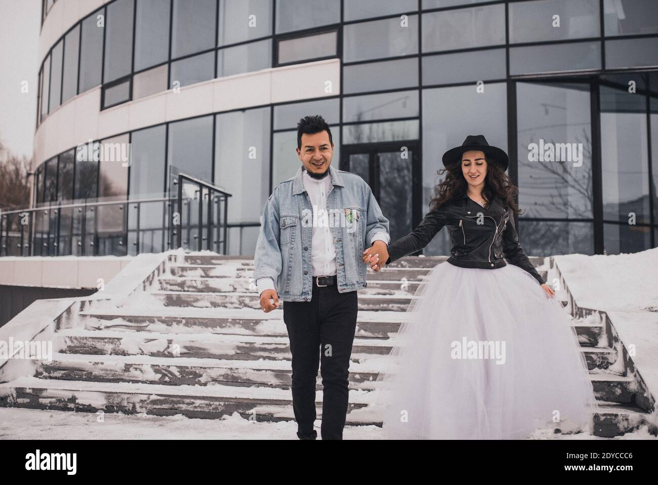 Mexikanische hispanischen Mann und Frau im Hut küssen Umarmung lachend zu Fuß. Bräutigam Braut Hochzeit Liebe Paar im Winter im Schnee auf dem Hintergrund von Shop wi Stockfoto