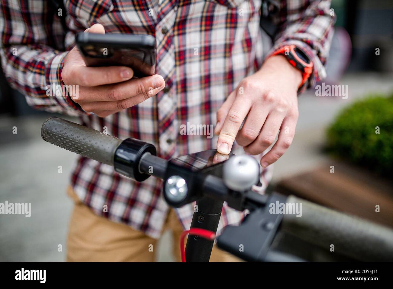 Männliche Hände modernen Elektroroller schaltet sich ein und Melodien. Kaukasischen Mann gekleidet stilvoll lässig verwendet Handy, um Kick Scooter zu steuern, close-up nein Stockfoto