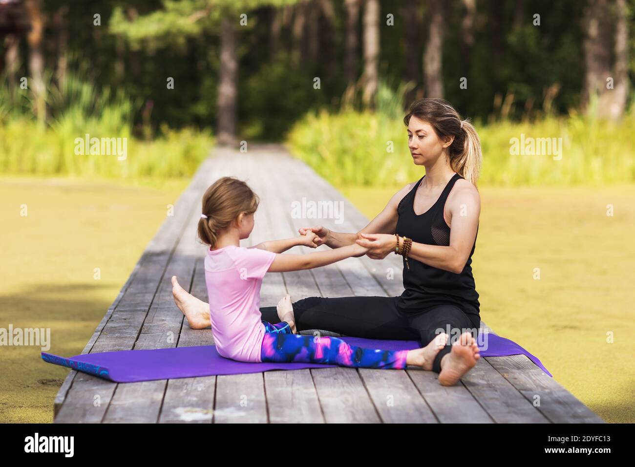 Mama und kleine Tochter machen Stretching-Übungen an einem sonnigen Sommermorgen in der Natur. Stockfoto