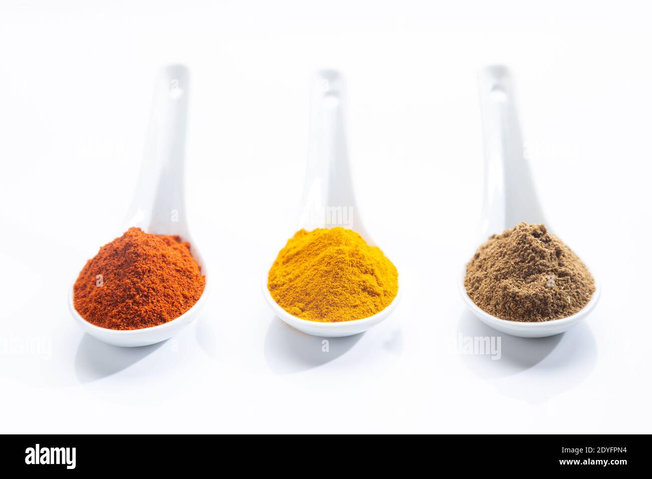 Drei weiße Löffel mit Paprika, Kurkuma und Kreuzkümmel auf weißem Hintergrund. Kochen Zutaten und Gewürze Konzept. Stockfoto
