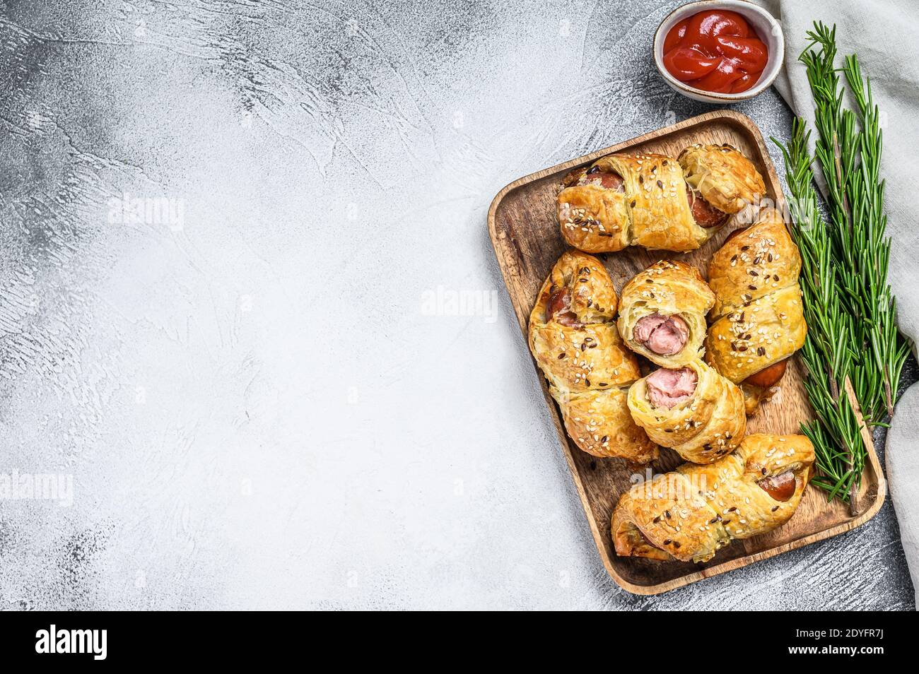 Holzplatte mit Würstchenrollen im Teig. Weißer Hintergrund. Draufsicht. Speicherplatz kopieren Stockfoto