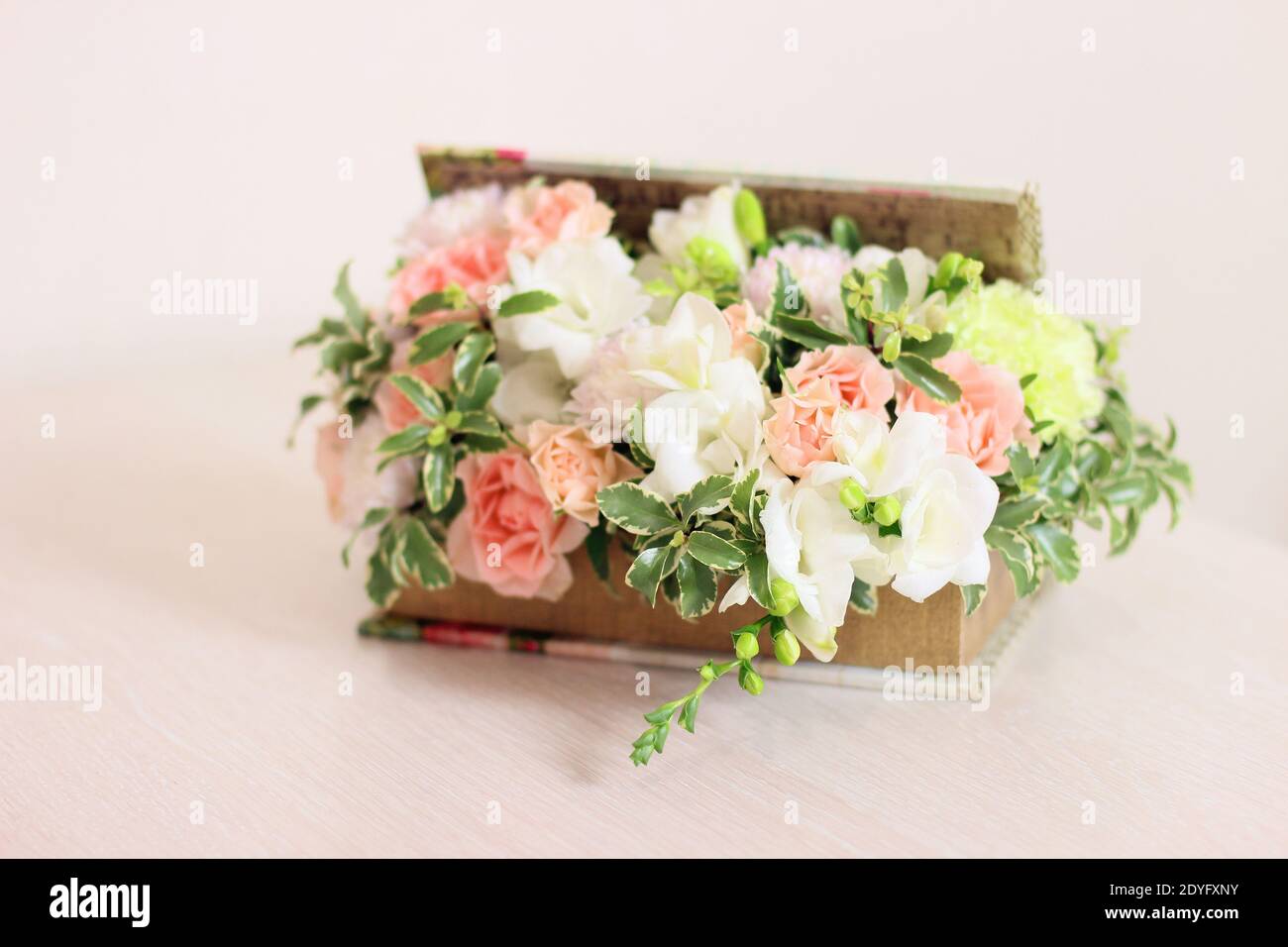 Schachtel Mit Duftenden Blumen. Die Komposition umfasst Pfirsichrosen, weiße Freesie, hellgrüne Dianthus, Chrysantheme und flauschige Grüntöne. Gif Stockfoto