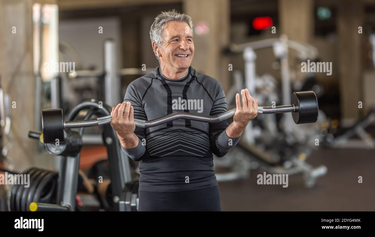 Mann in grauen Haaren zieht Gewichte in der Turnhalle. Stockfoto