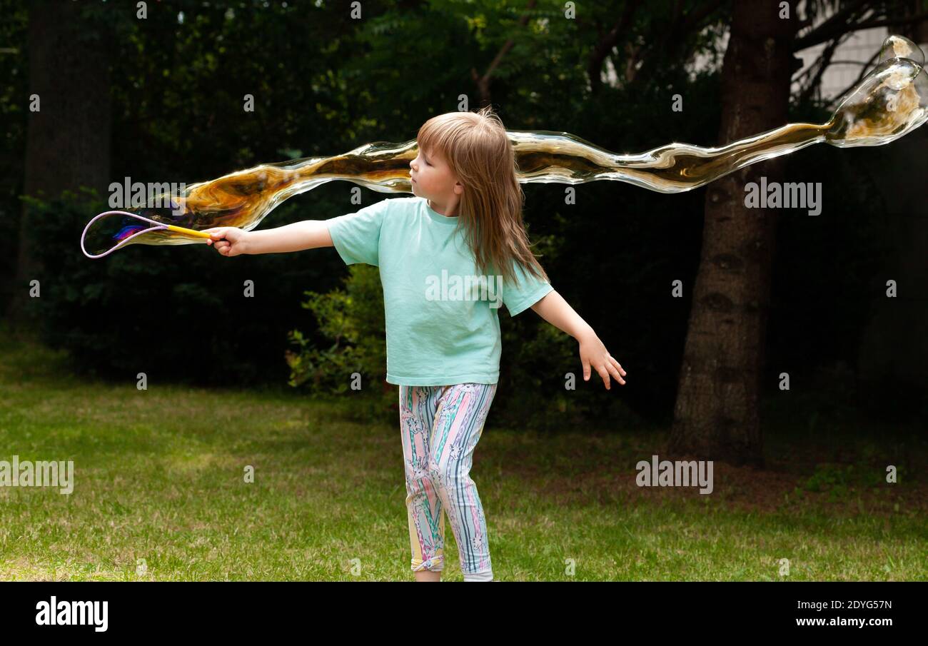 Ein kleines Kind, kleines Mädchen, das riesige Seifenblasen im Garten macht. Aktives Kind im Hinterhof, grünen Park weht große gigante Blasen, Spaß haben Stockfoto