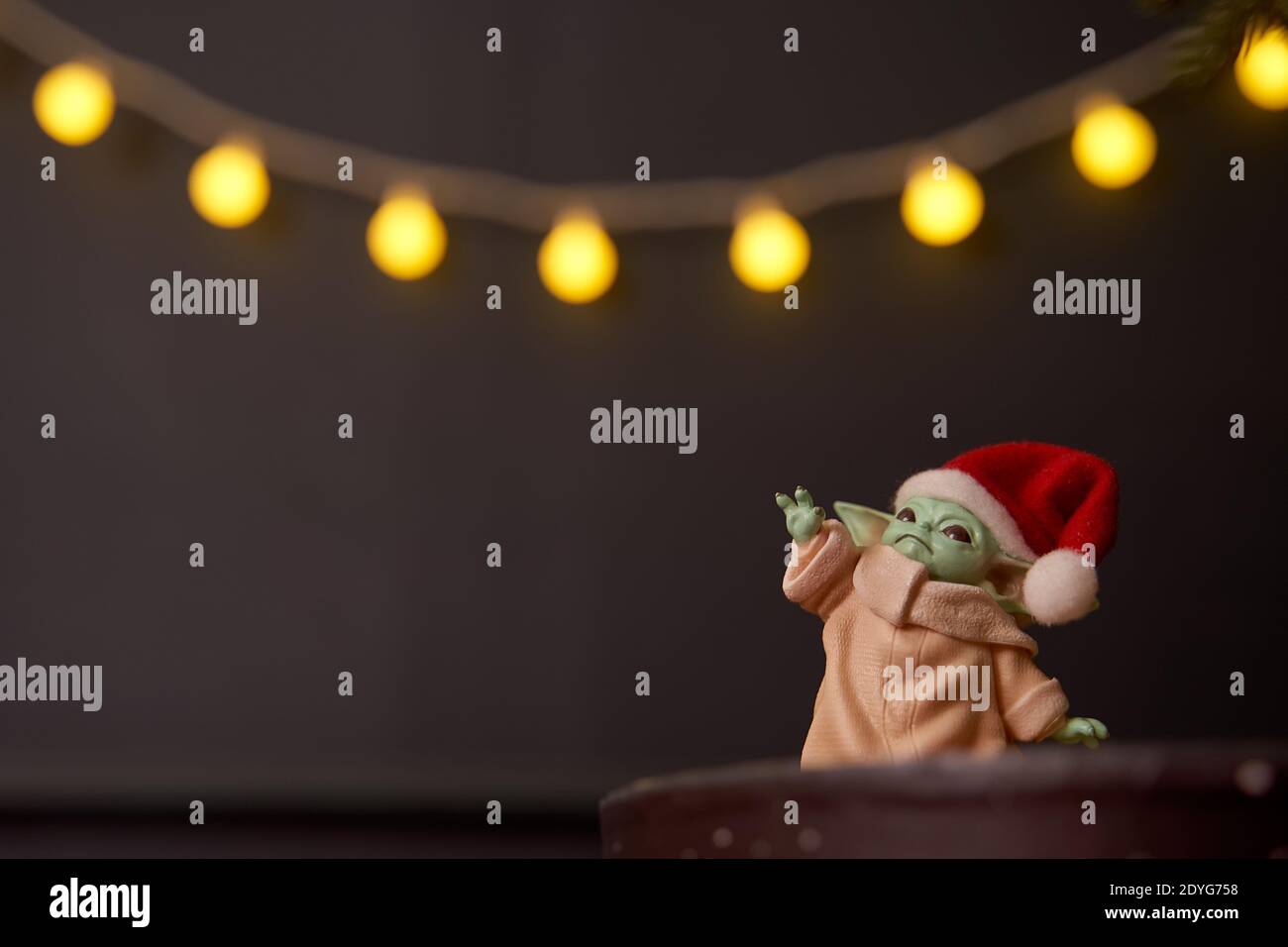 Dez, 2020: Darstellung von Baby Yoda, einer Action-Figur, die in einer roten Mütze auf weihnachtlichem Hintergrund steht. Bokeh-Effekt. Stockfoto