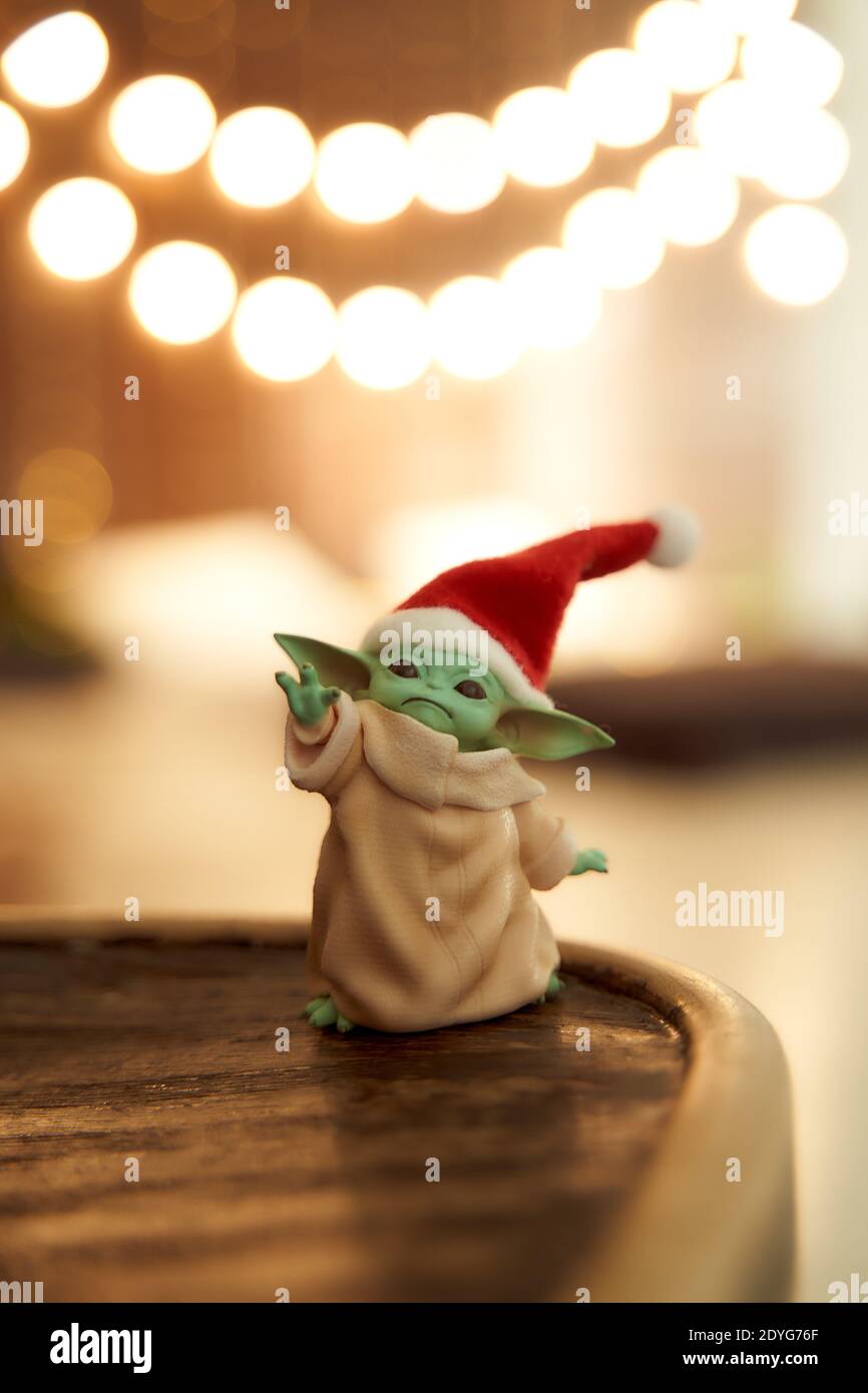 Dez, 2020: Darstellung von Baby Yoda, einer Action-Figur, die in einer roten Mütze auf weihnachtlichem Hintergrund steht. Bokeh-Effekt. Stockfoto