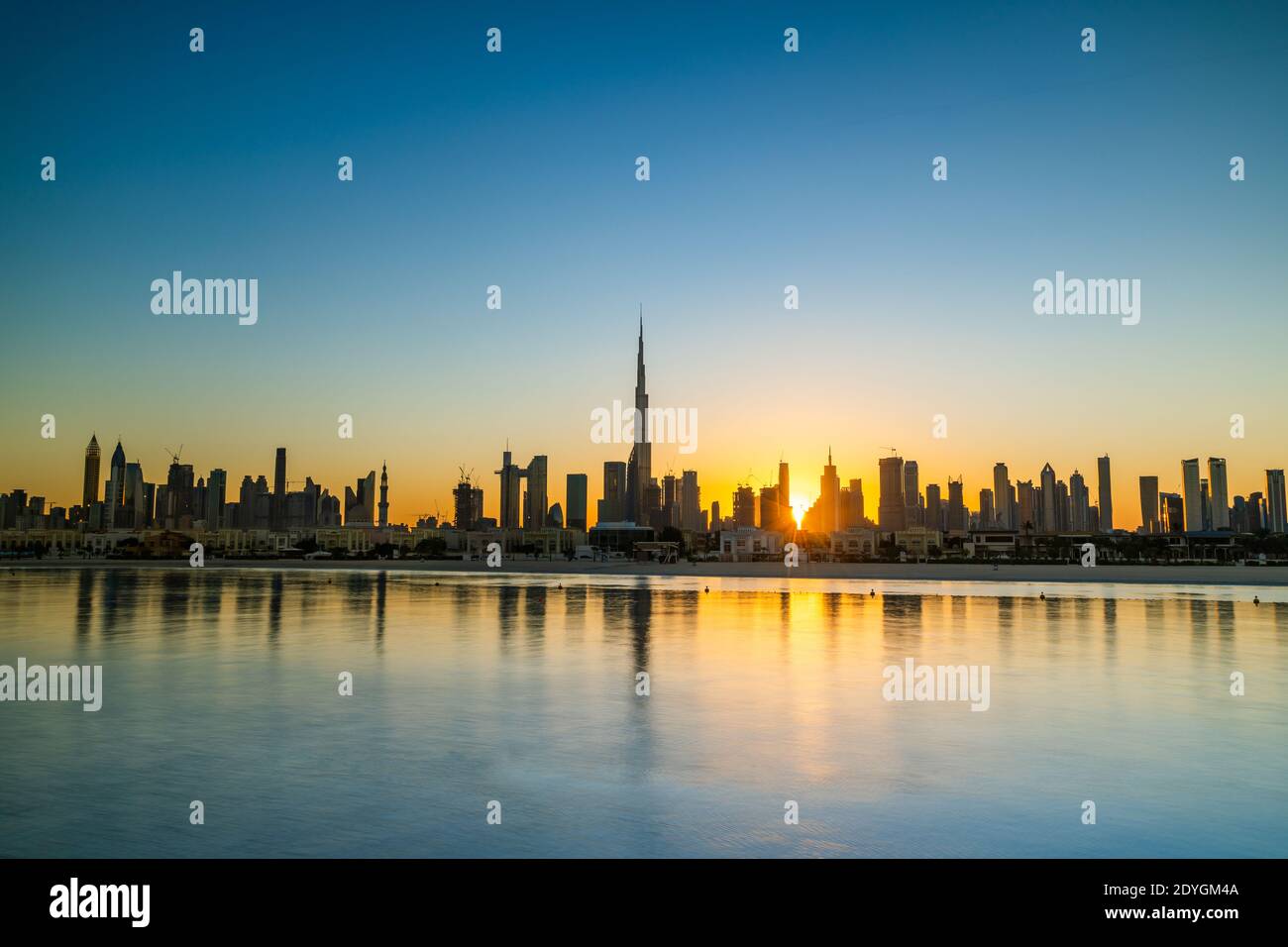 Sonnenaufgang in Dubai mit klarem blauen Himmel Blick vom Boot oder Meer. Morgens geht die Sonne über den Wolkenkratzern der VAE auf. Dubai Strand, Küste, Ufer Stockfoto