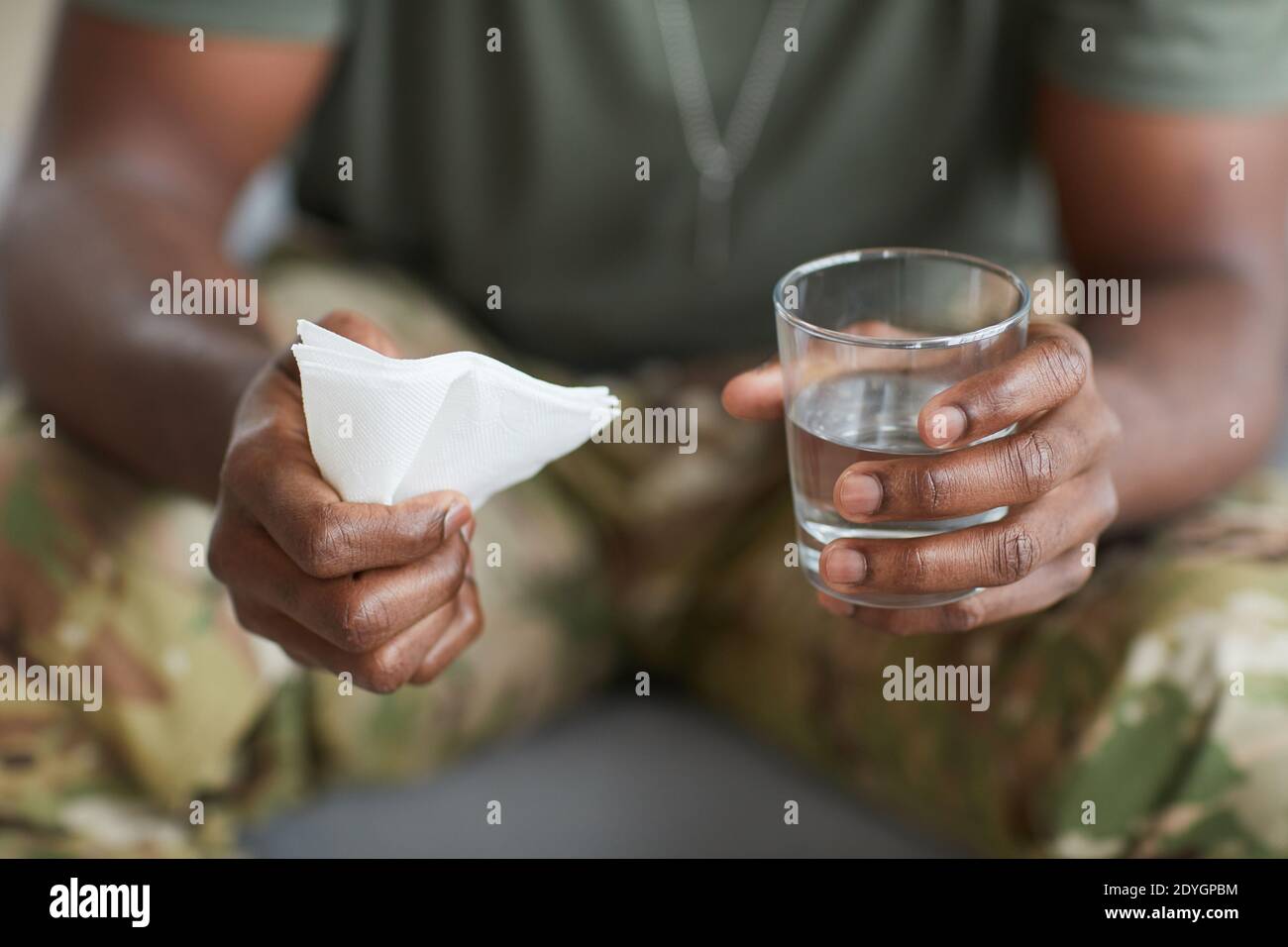 Nahaufnahme eines afrikanischen Mannes, der mit einem Glas Wasser sitzt und Serviette in den Händen Stockfoto