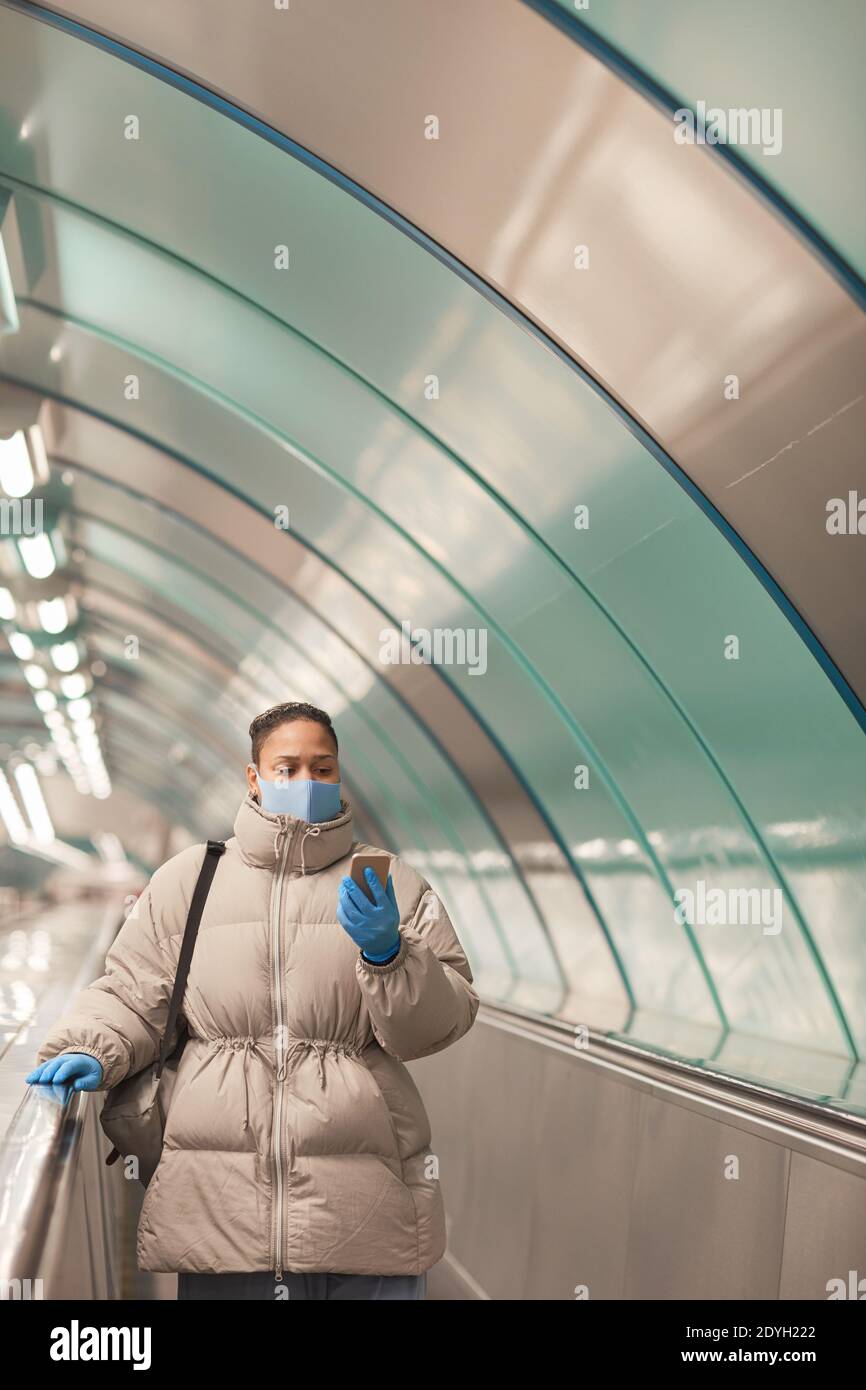 Junge Frau in Schutzmaske und Handschuhe mit ihrem Handy Telefon, während Sie auf der Rolltreppe stehen Stockfoto