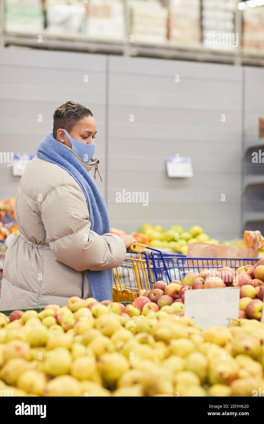 Junge Frau in warmer Kleidung und in Maske kaufen frisch Obst im Supermarkt Stockfoto