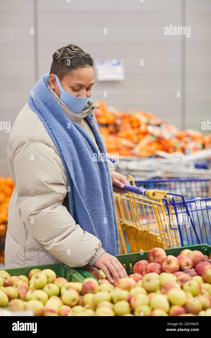 Junge Frau in warmer Kleidung und in Maske Auswahl frisch Obst im Supermarkt Stockfoto