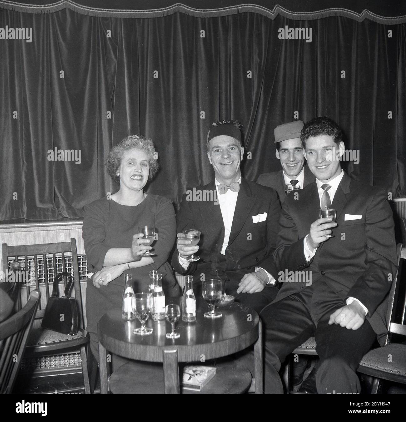 1950er Jahre, historisch, bei einer abendlichen gesellschaftlichen Veranstaltung in einem Ballsaal, lächelt rundum, wie Mutter und Vater, zwei in Partyhüten zelerieren und heben ein Glas, sitzen mit ihren beiden Söhnen, England, Großbritannien, an einem kleinen Tisch. Stockfoto