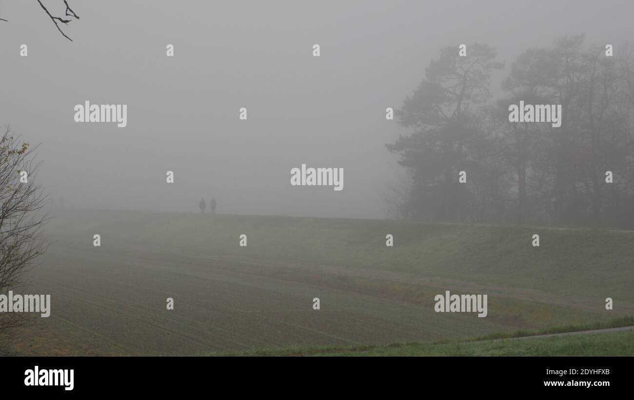 Zwei einsame Menschen im Nebel eines nebligen Morgens Gehen auf einem Deich während der Coronapandemie Stockfoto