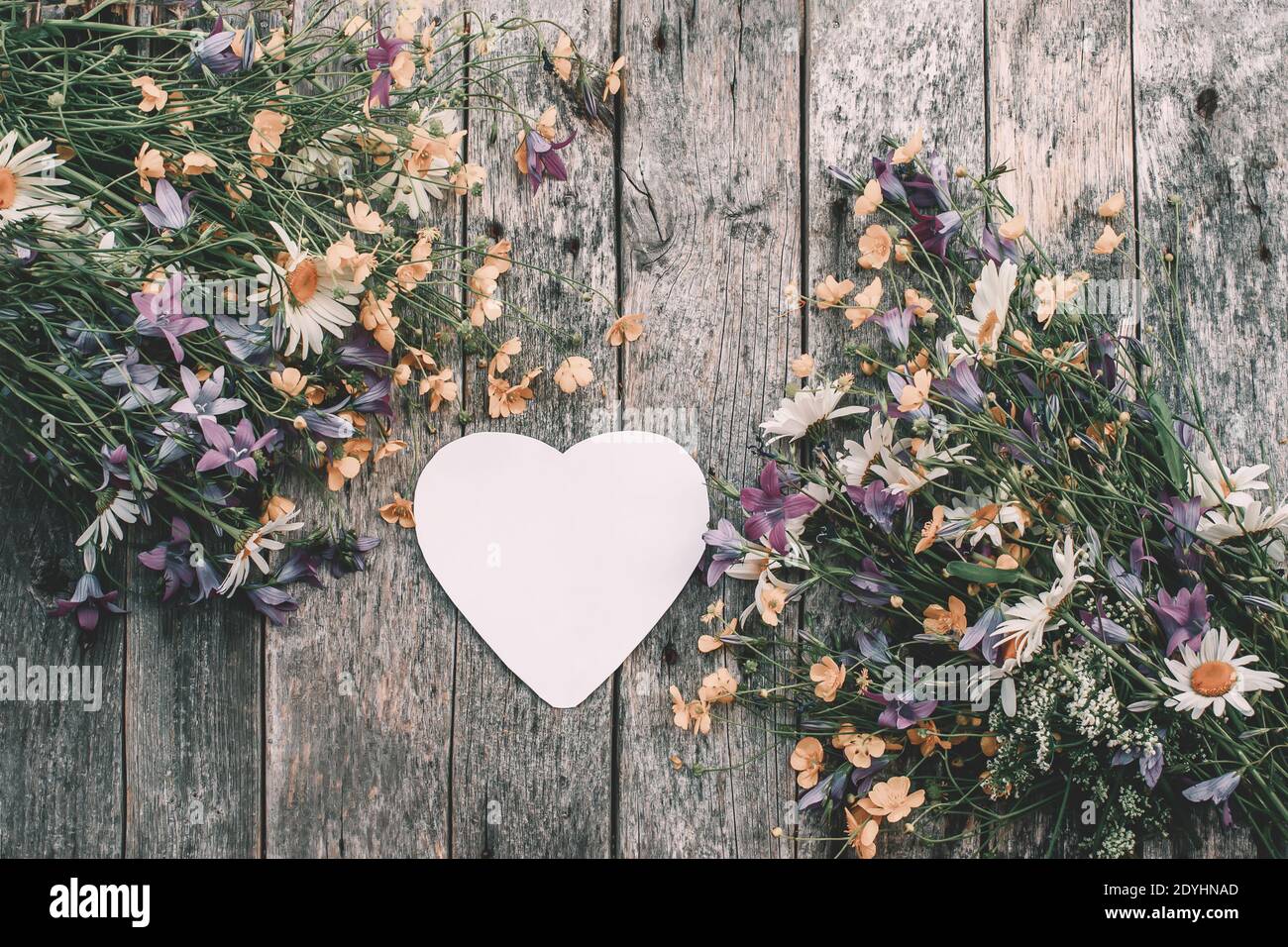 Schönes Bouquet von hellen wilden Blumen mit einem Herzen in Form einer Notiz für Text auf einem Holzbrett. Ein Bild mit einem weichen, selektiven Fokus. Valenti Stockfoto