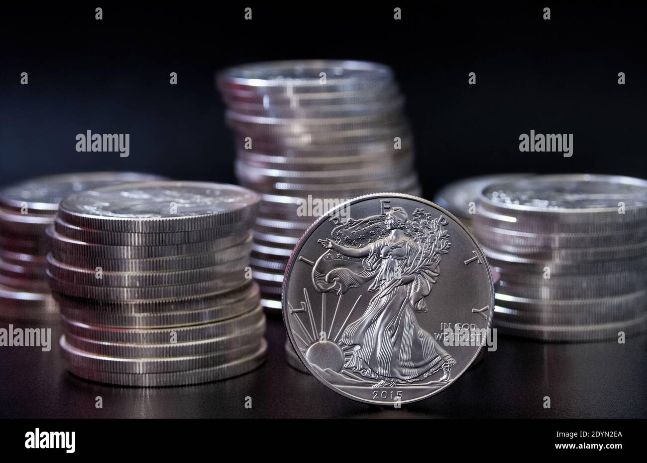 Eine einzelne Silbermünze des amerikanischen Adlers, die aufrecht vor dem steht Stapel von American Eagle Dollar Silbermünzen Stockfoto
