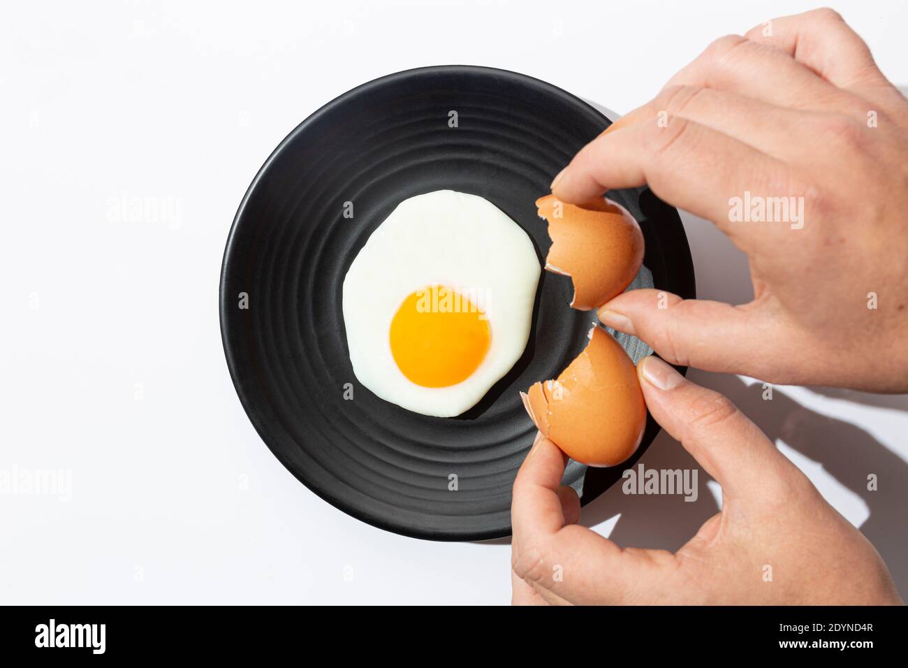 Hände knacken Gebratene Ei auf schwarzem Teller auf weißem Hintergrund. Kochen und Essen Konzept. Stockfoto