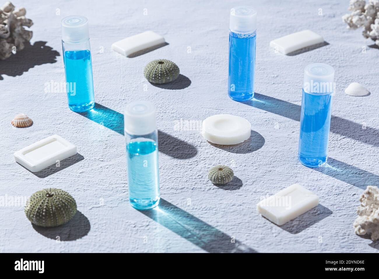 Blaue und weiße Shampoos und Seifen für die Körperpflege, auf weißem Hintergrund, mit Korallen und Muscheln. Stockfoto