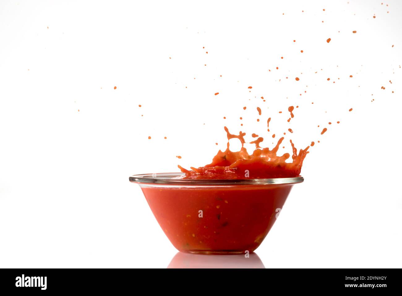 Tomatensauce spritzt aus Glasschüssel, isoliert auf weißem Hintergrund Stockfoto