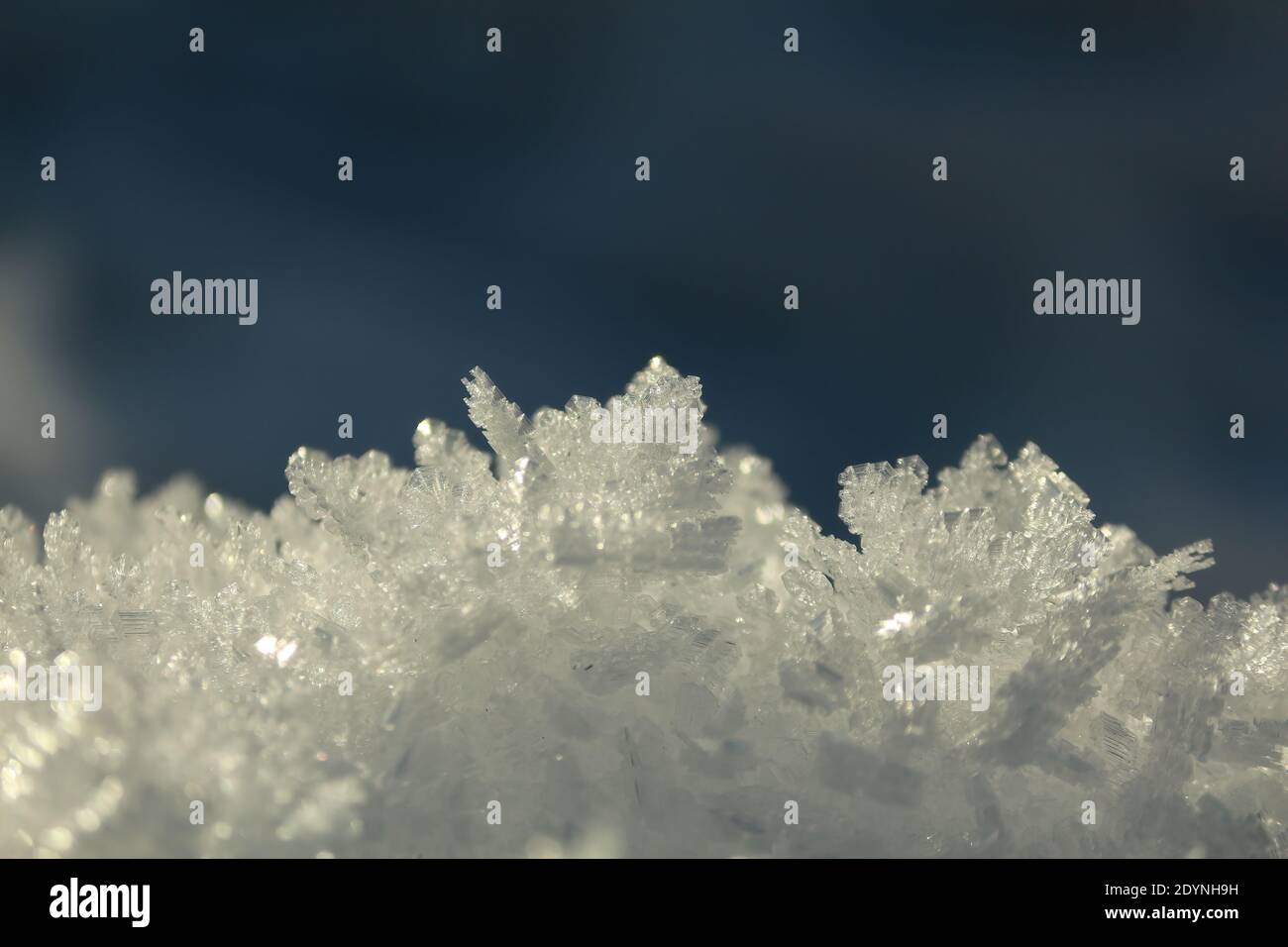 Abstraktes Schneekristalle-Muster. An einem Wintertag funkelt eine Oberfläche aus kristallisiertem Frost in der Sonne gegen einen blauen Himmel. Winter natürlicher Hintergrund. Stockfoto