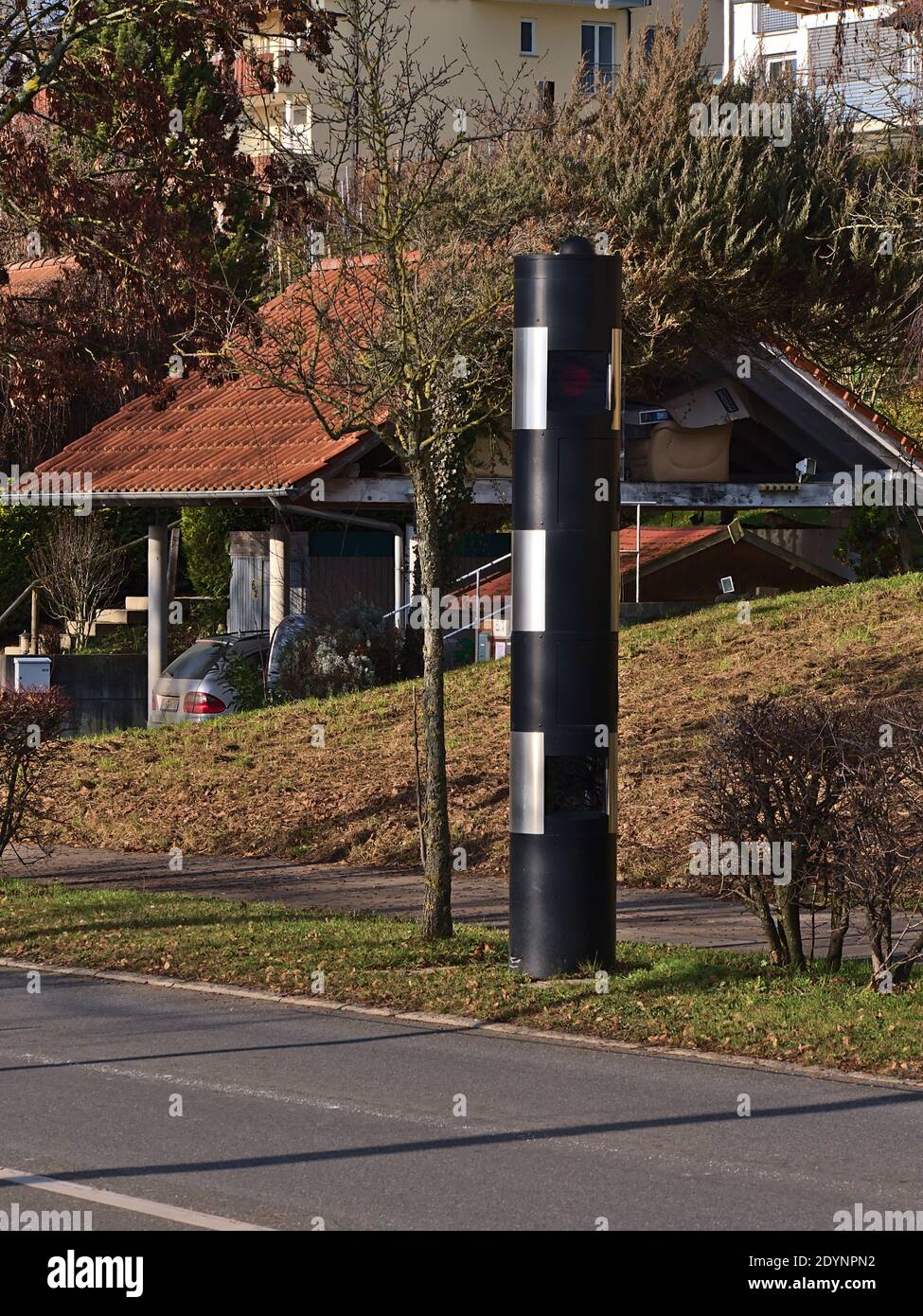 Moderne schwarz gefärbte Verkehrsdurchsetzungskamera für Geschwindigkeitskontrolle am Dorfeingang mit Straße vor an sonnigen Wintertag. Stockfoto