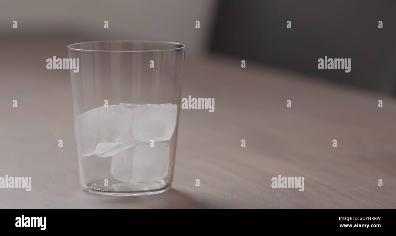 Fügen Sie Eis in Glas Tumbler auf Walnusstisch mit Kopierraum, breites Foto Stockfoto