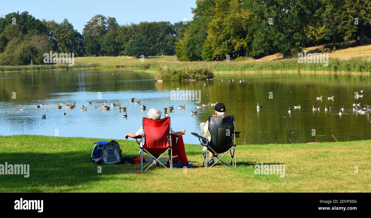Paar sitzen auf Stühlen Blick auf einen See mit Enten und Bäume Stockfoto